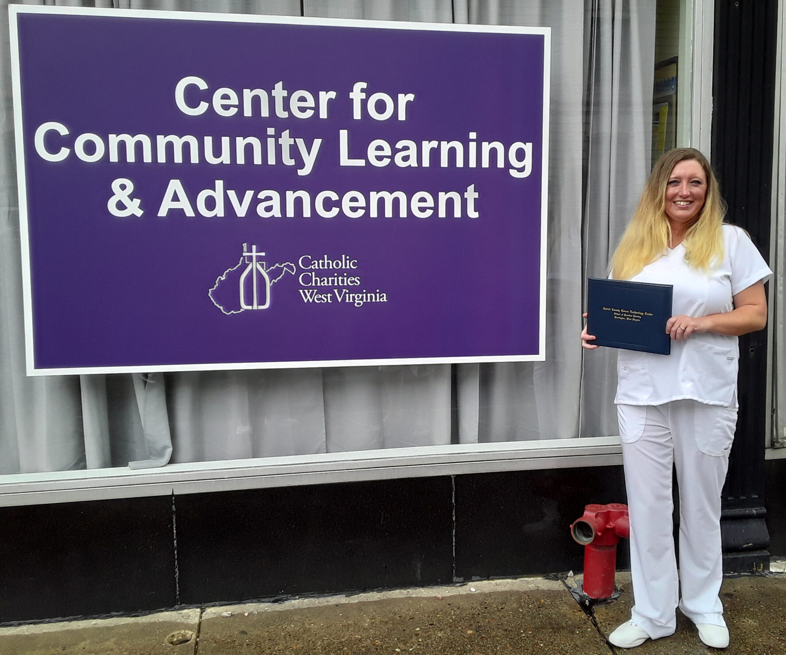 Debra Bunch, dressed in her graduation whites, holds her Licensed Practical Nurse diploma